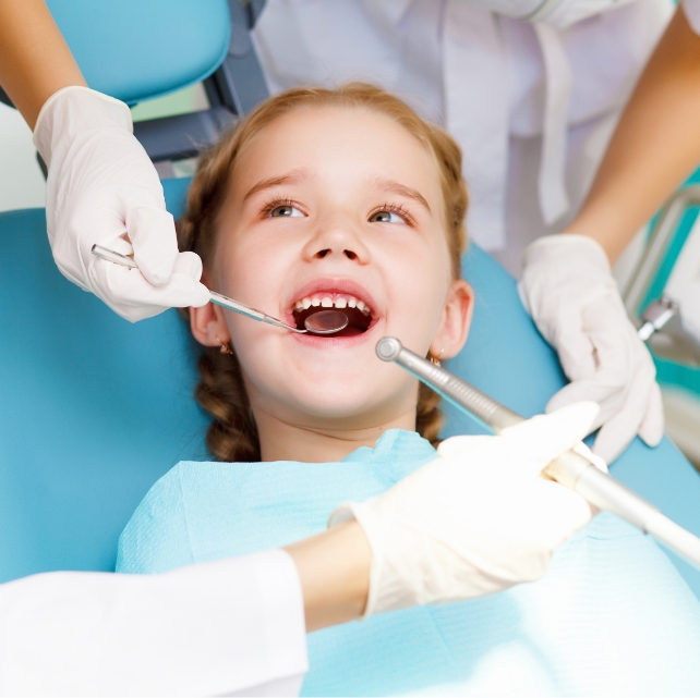 Child sitting in the patient chair with a dental hygienist and a dentist.