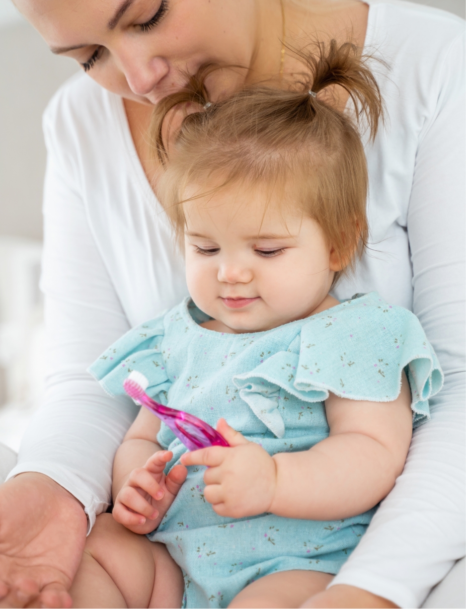 little baby looking at a toothbrush and learning how to take care of her dental health after a visit to the dental clinic