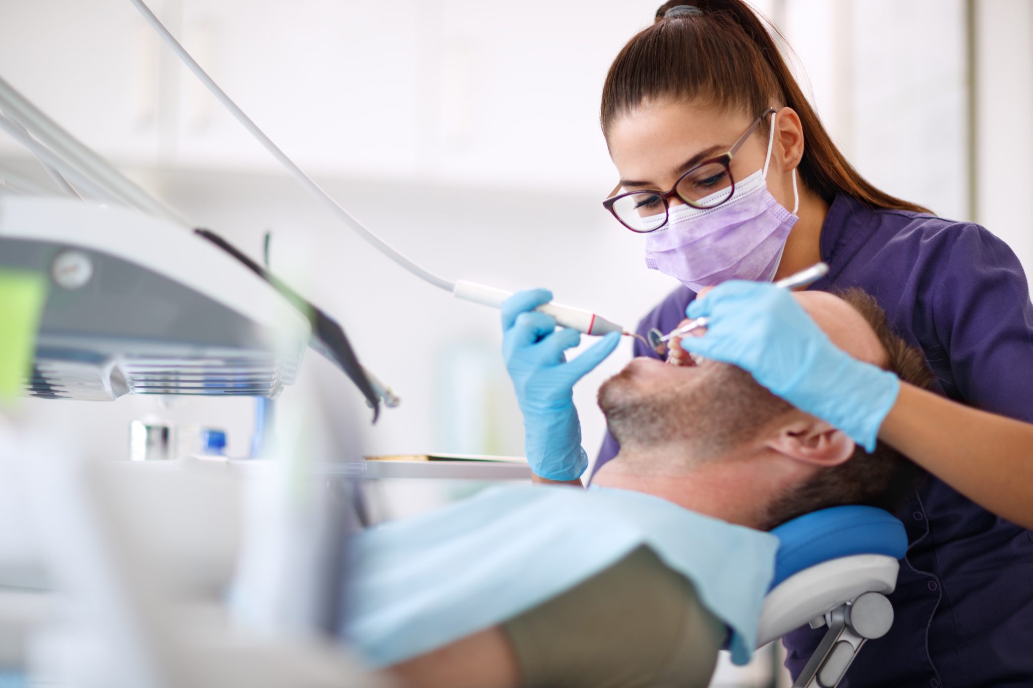 Female dental hygienist using a drill on a male patient in a dental chair